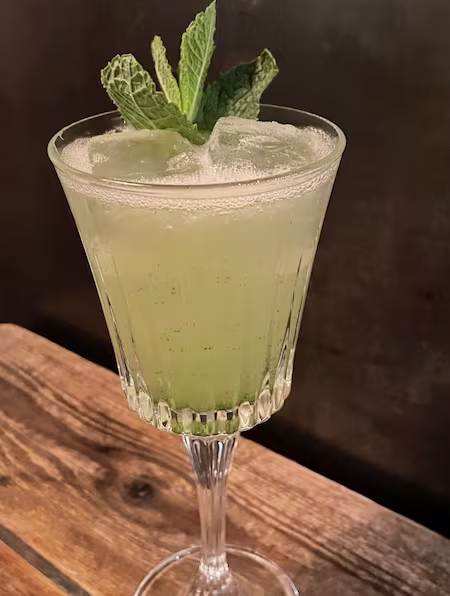Timeless Glassware Filled With Green Color Liquid Mint Leaf As Garnish On Wooden Table